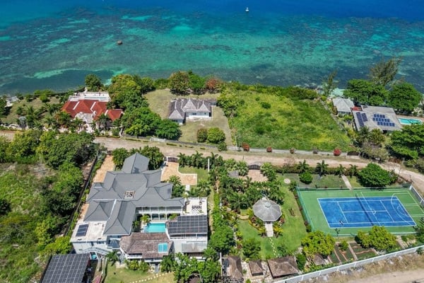Aerial view of beachfront villa with pool, tennis court, and turquoise ocean water