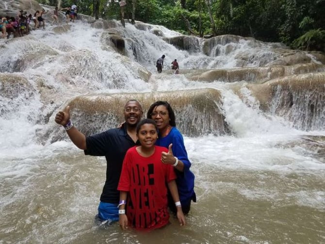 Family of three posing in shallow water at terraced limestone waterfalls surrounded by lush forest