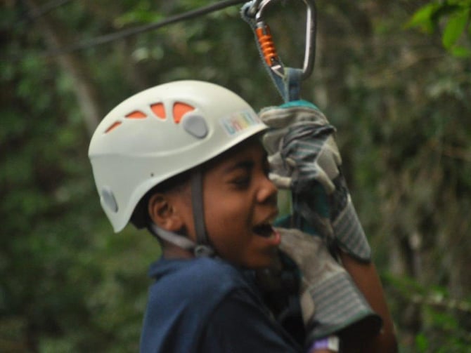 Person wearing white climbing helmet and harness on zipline through forest canopy